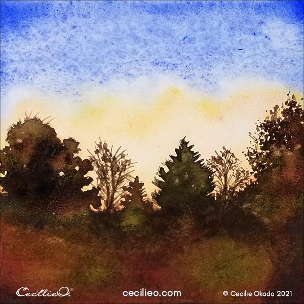 The completed watercolor sunset with a blue and golden sky, and silhouette trees.